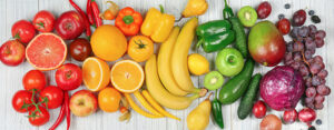 Colorful assortment of fruits and vegetables arranged on a white wooden surface.
