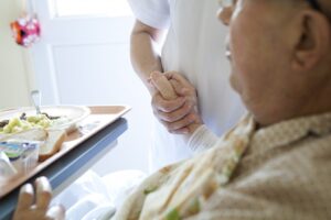 Hospice care: Nurse holds elderly patient's hand beside a meal tray.