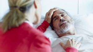 Woman comforts elderly man in hospice care, lying in bed. Support for end-of-life care.