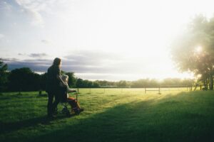 Woman pushing elderly person in wheelchair through grassy field; hospice care.