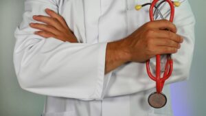 Doctor in white coat holding a red stethoscope, related to hospice care.