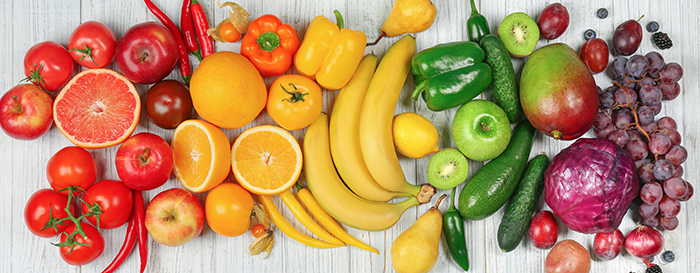 Colorful assortment of fruits and vegetables arranged on a white wooden surface.