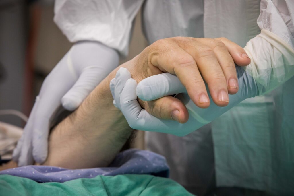Hand of a COVID-19 patient being held by a healthcare worker wearing gloves.