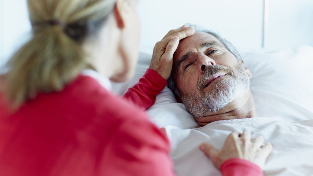 Woman comforts elderly man in hospice care, lying in bed. Support for end-of-life care.