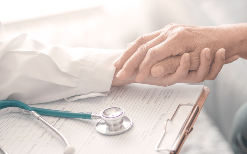 Doctor holding patient's hand over discharge papers and a stethoscope. Palliative care and compassion.