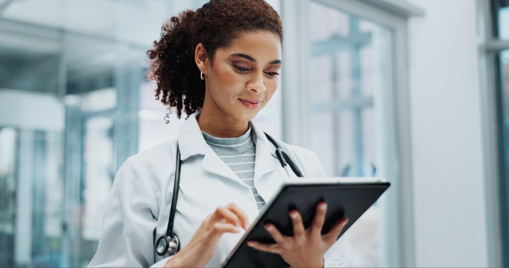 Doctor with white lab coat on and stethoscope reviewing and working on tablet.