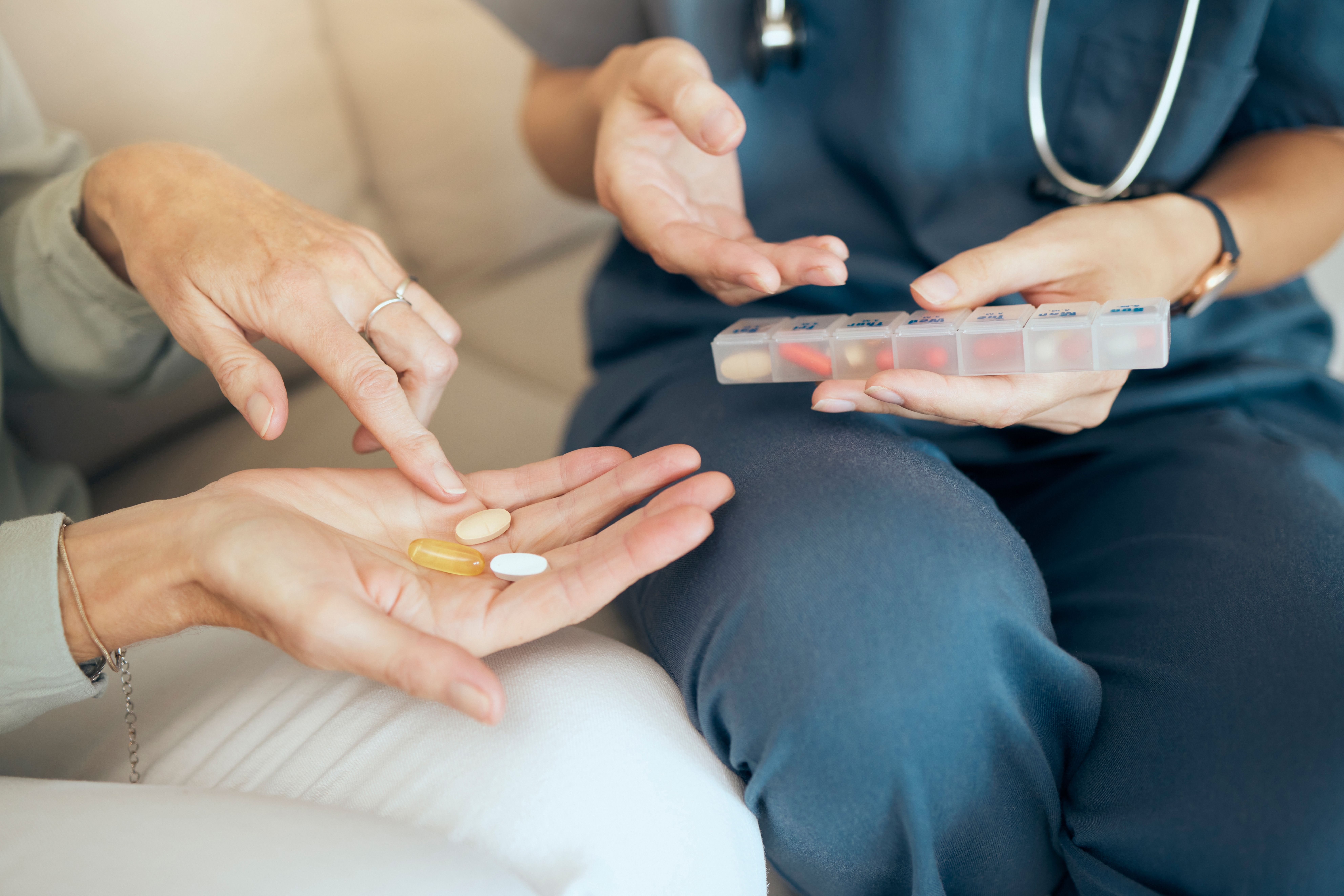 Caregiver with medication organizer giving pills to senior patient.