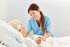 Caregiver smiling at elderly woman in bed, providing hospicecare at home.