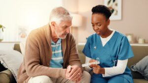 Home health aide assisting senior man with medication management using a pill organizer.
