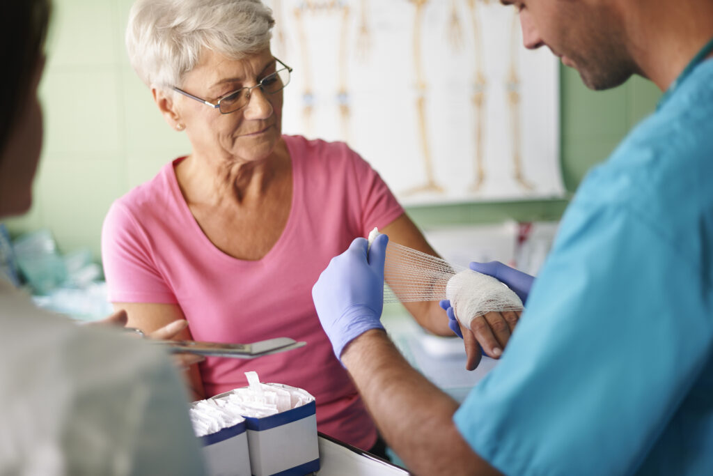 Doctor bandaging elderly woman's hand in a hospice care setting. Medical professional providing wound care.