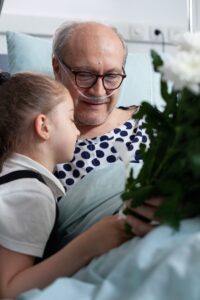 Little girl hugging senior man while laying in hospital bed with supplemental oxygen.